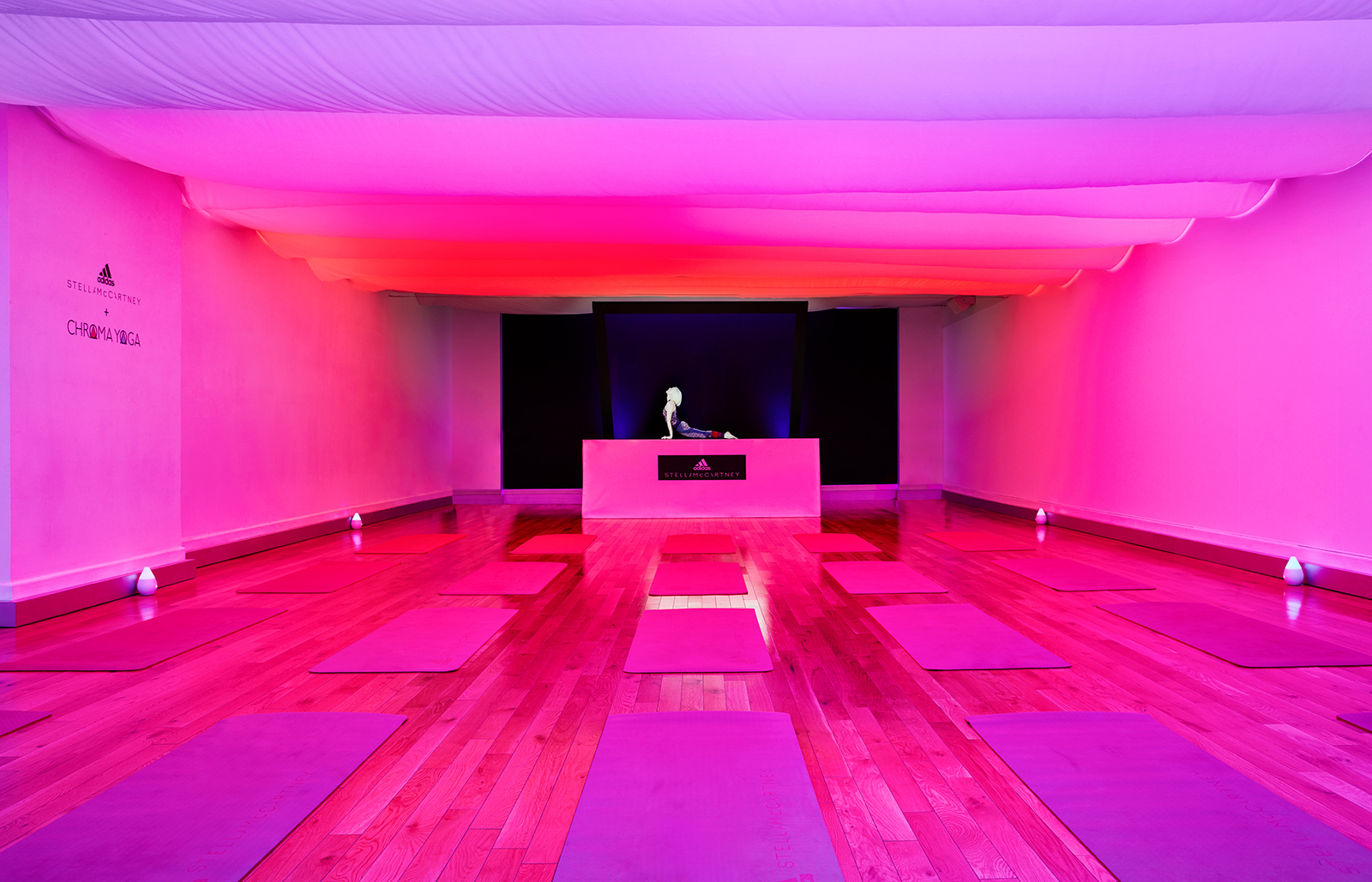 A pink and red lit space set up with yoga mats and a hologram instructor at the front of the room.