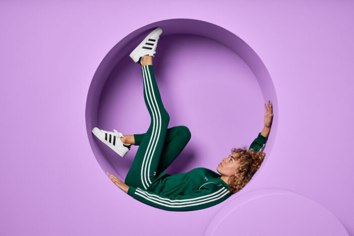 Woman wearing all emerald green reclines in a circular cutout in a lavender-purple wall.