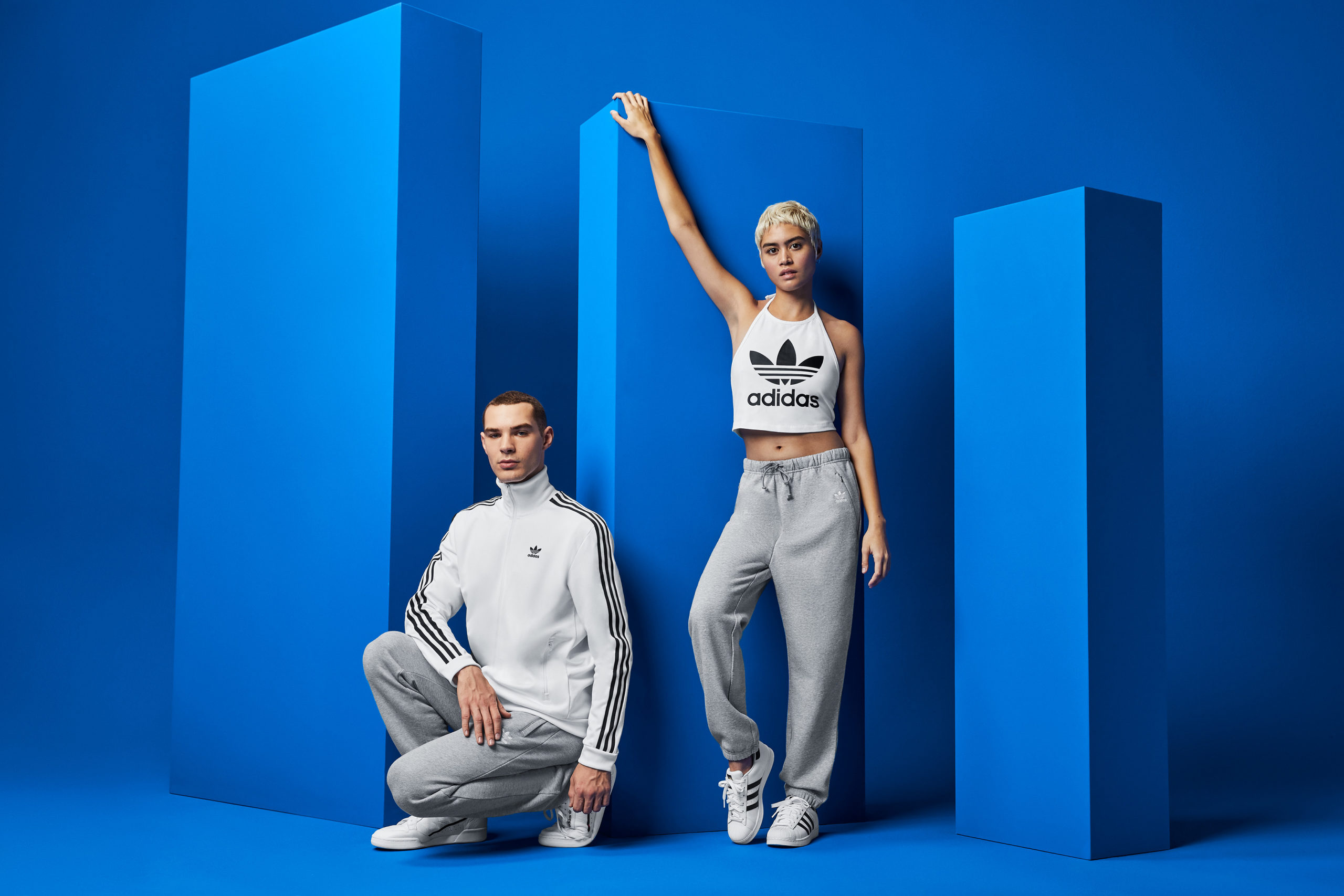 Two models, in white and gray, kneel and stand in a blue set in front of three blue modular towers.