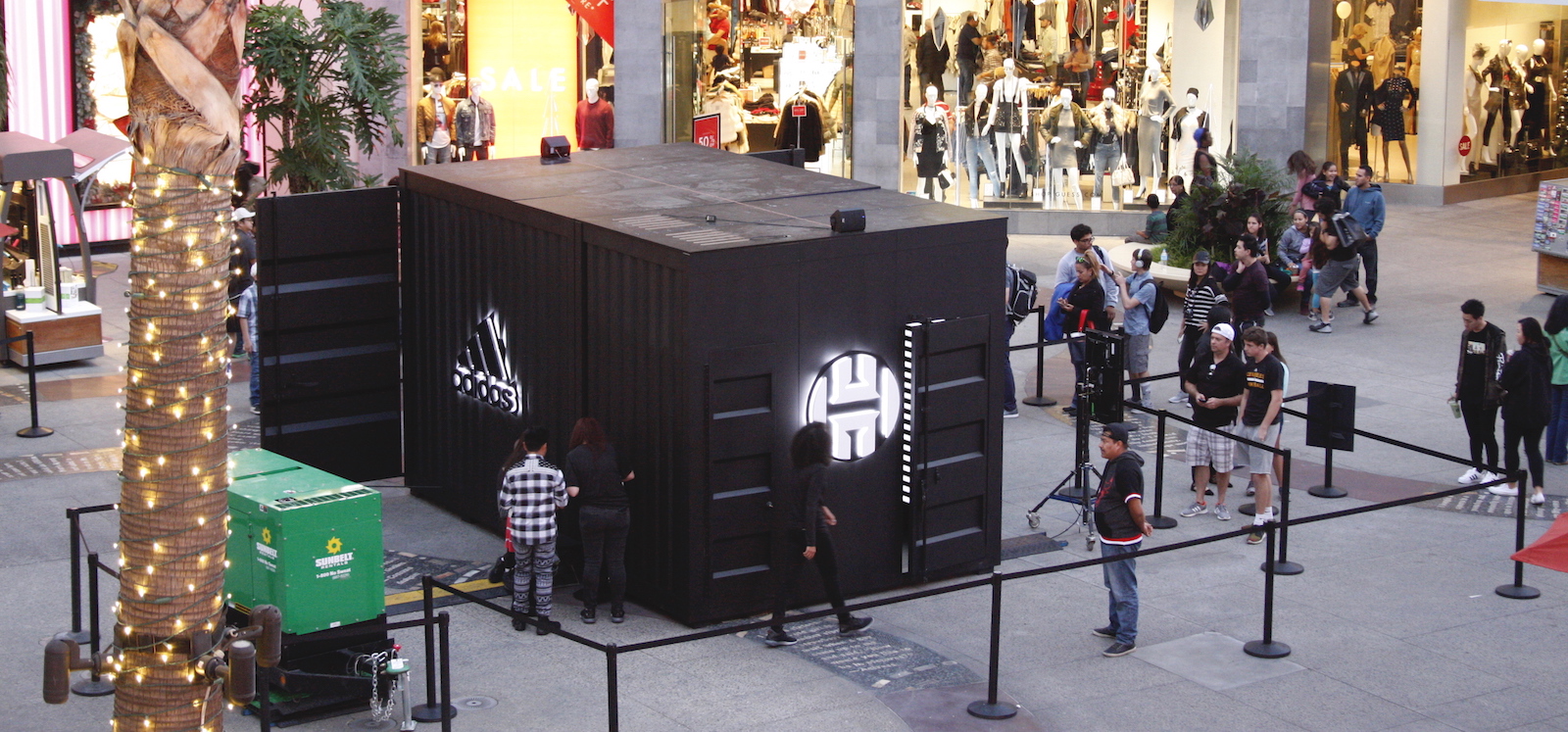 An aerial view of the activation pod which is a large black shipping container with large lit adidas and Harden logos, and a door cracked open to reveal a black and white striped glowing interior.