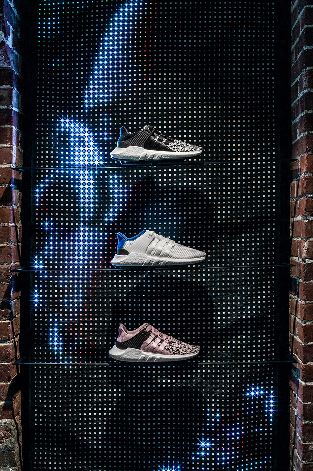 A closeup of three sneakers posted in front of a profile of a face shown on the LED curtain.