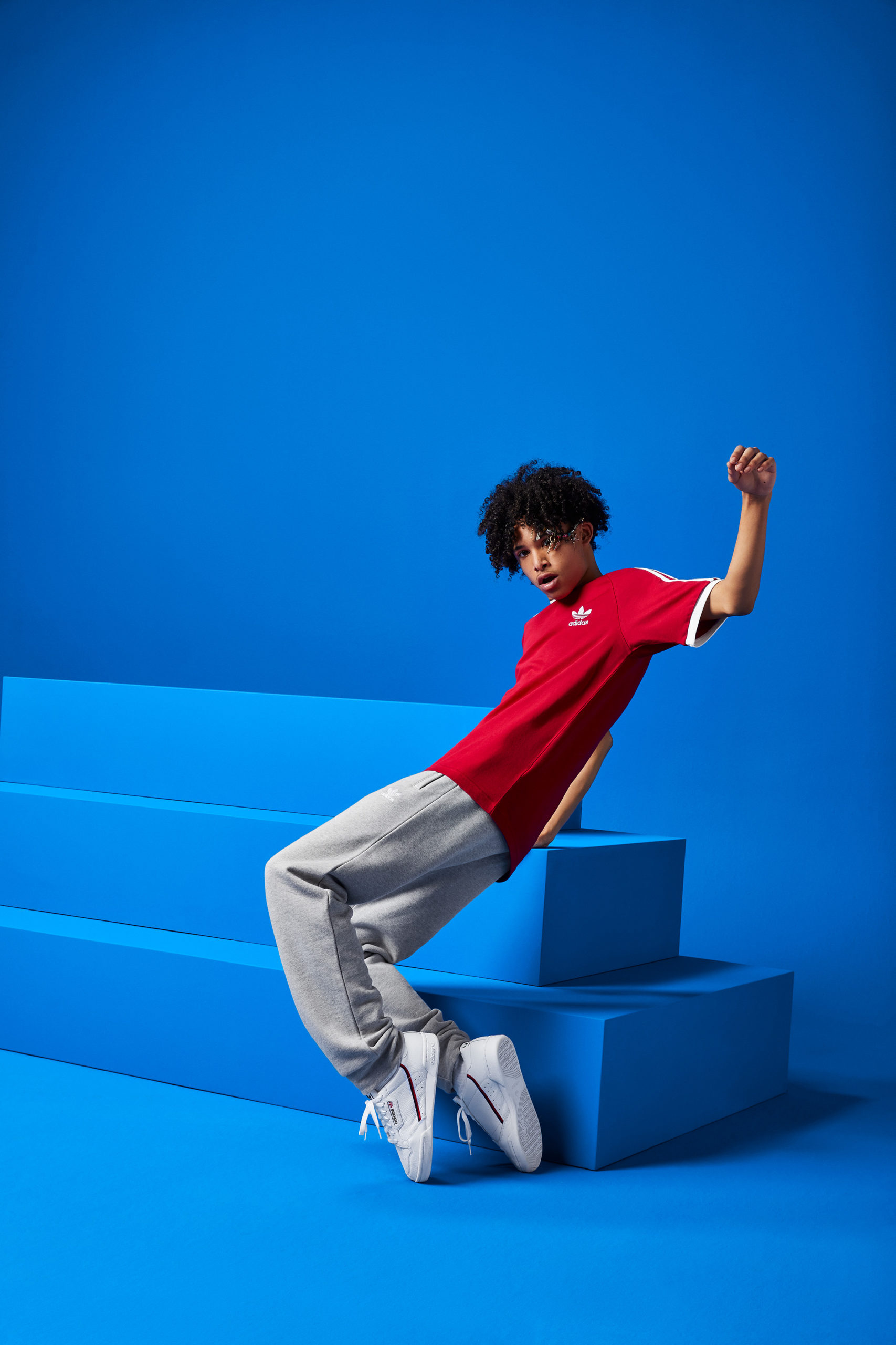 A guy wearing a red shirt dances in front of a blue set with a stack of stair-stepped boxes.