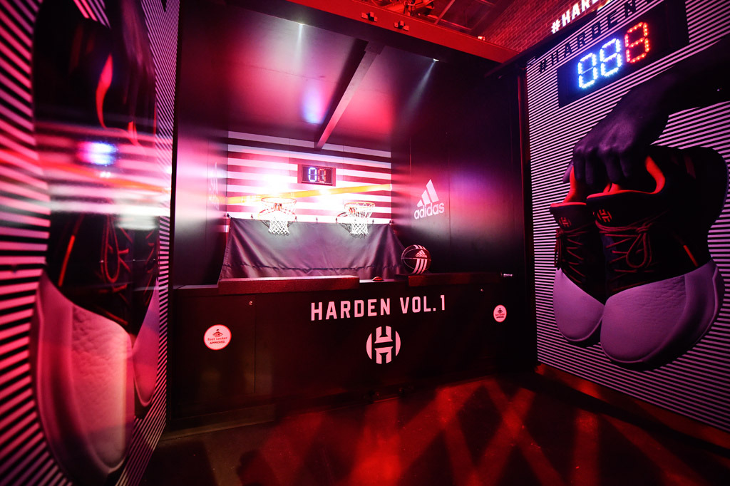 A view of the pop-a-shot game customized with adidas and Harden branding, and immersive black and white striped wall graphics showing a hand holding a pair of the shoes.
