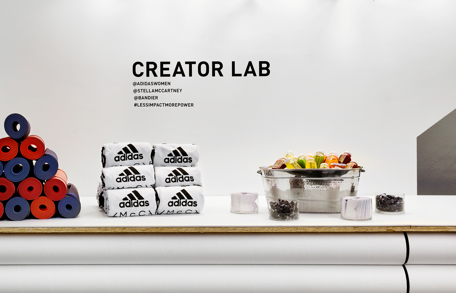 A stack of yoga mats, branded towels, and some snacks and juices sit on a white counter with Creator Lab written on the wall behind.