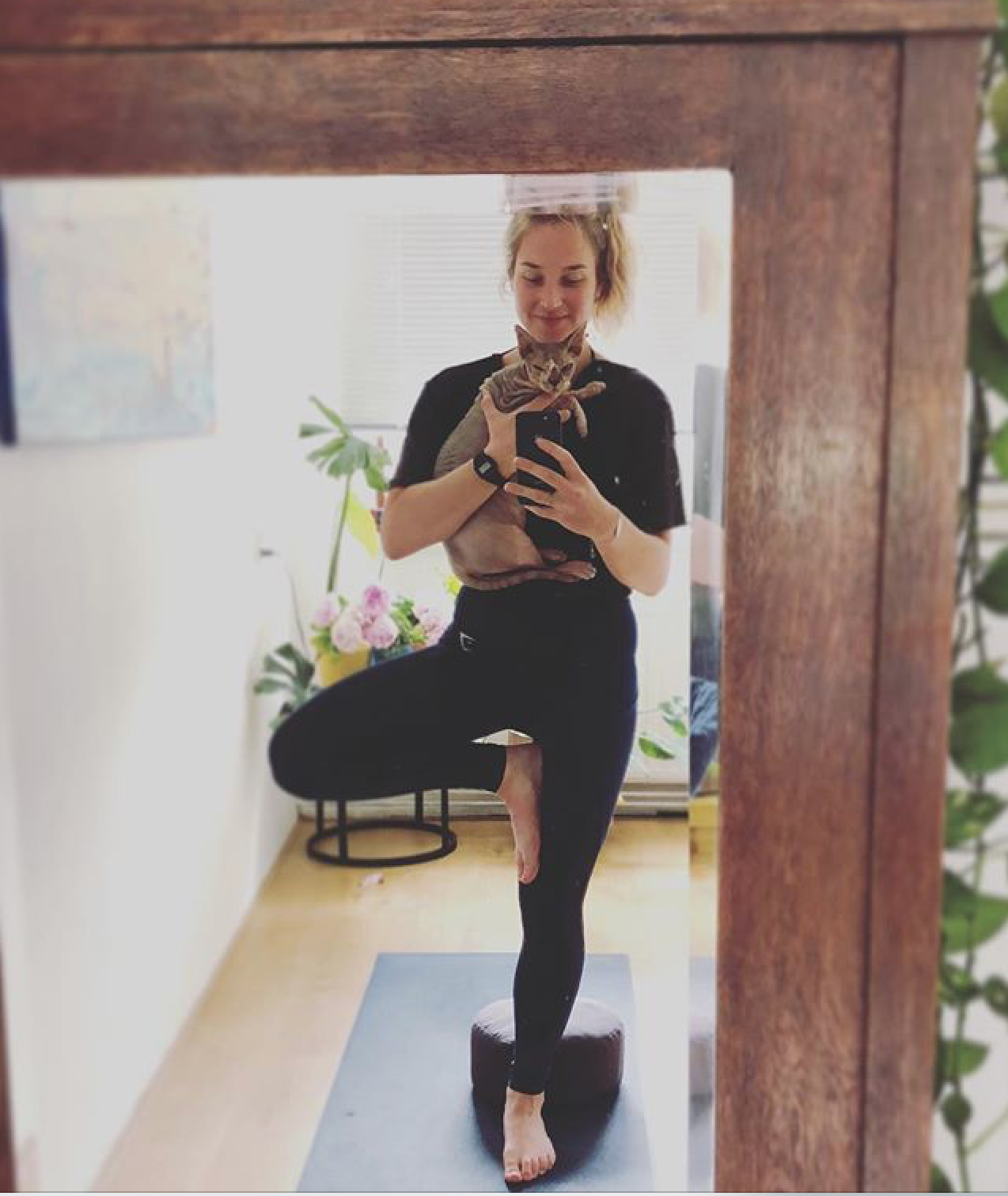 A woman does tree pose with her hairless cat in her home.