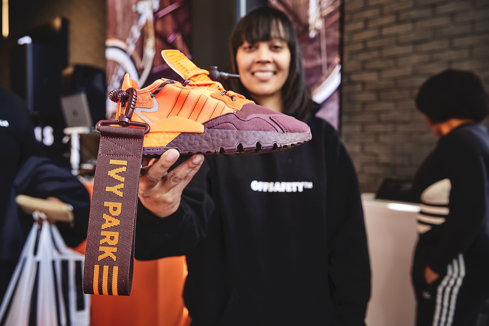 A guest holds up an orange and burgundy Ivy Park sneaker.