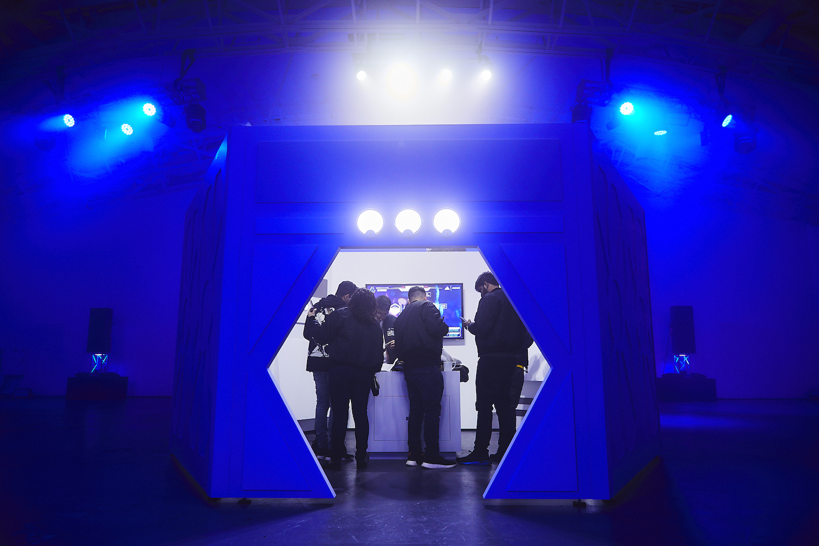 A group of people gather to work on the Space Race puzzles inside what looks like a spaceship control room, low-lit in blue on the outside and brightly lit on the inside.