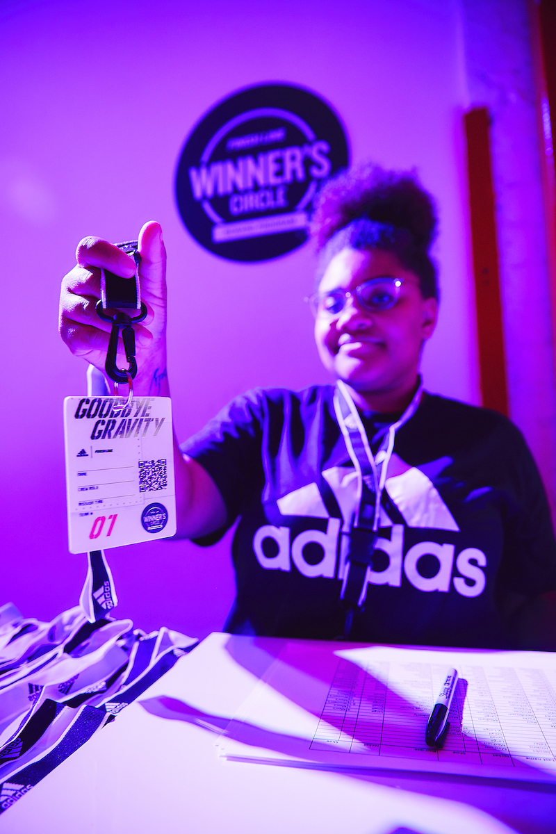 A person at a check-in desk holds up an event badge that reads Goodbye Gravity