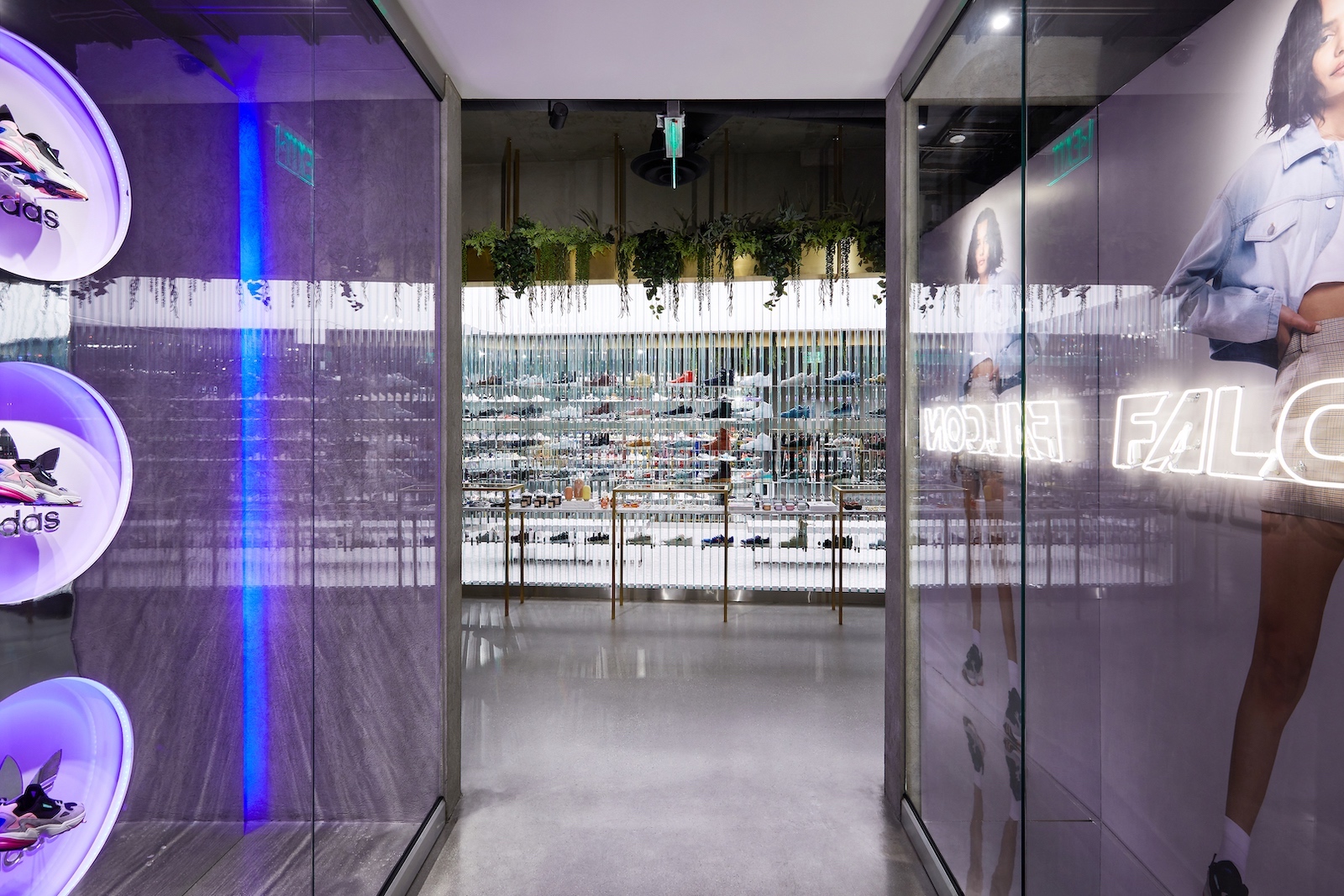A hallway with three Falcon sneakers displayed in purple-lit circular cutouts on the left and campaign imagery with neon signs reading Falcon on the right. A wall of sneakers is at the end of the hall.