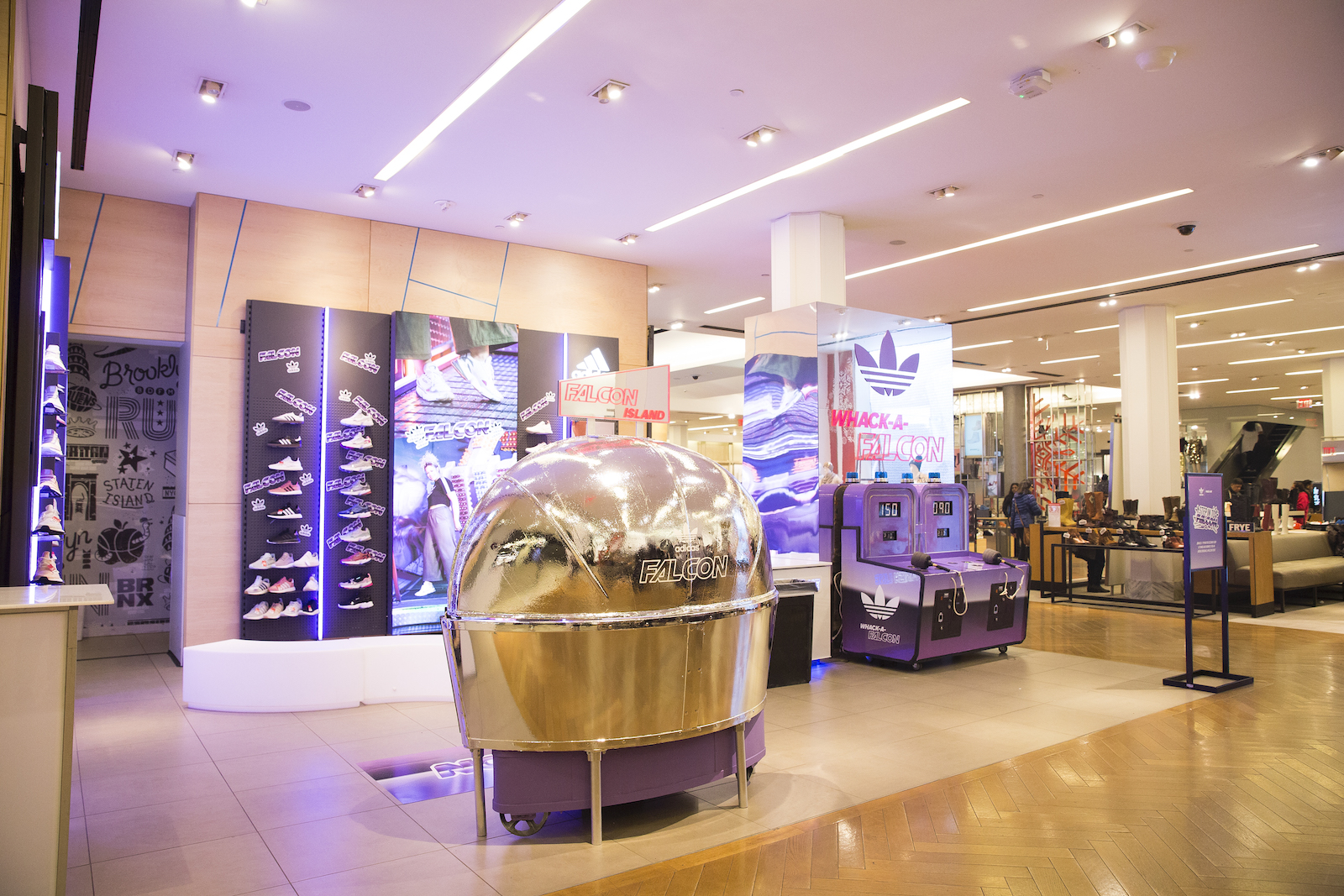 Another view of a retail space with a shoe wall with Falcon stickers, sneakers and  large campaign imagery, a round mirrored booth photo op, and two Whack-a-Falcon arcade games.