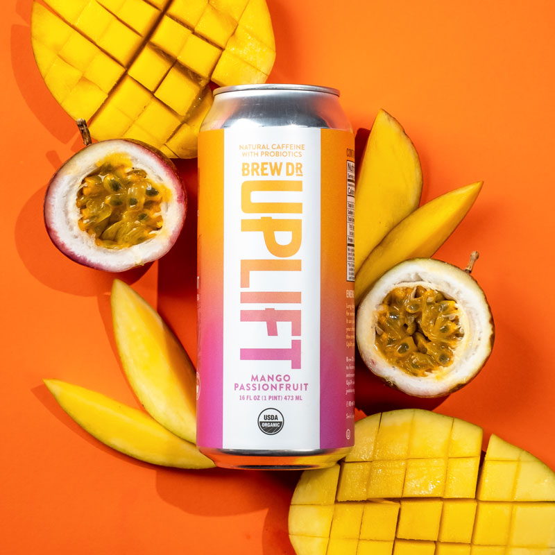 The Mango Passionfruit can on an orange background with slices of mango and a passion fruit cut in half.