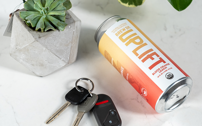 A can of Uplift laying on its side on a marble table top next to a small plant and a set of car keys.